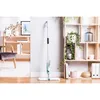 A spray mop is shown standing upright against a wall next to a bookshelf filled with plants and decorative items. Náhled obrázku produktu