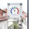 A humidity meter is attached to a window with a blurred background of houses. Produktbild-Vorschau