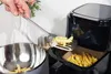 A hand is using a spatula to place french fries into an air fryer basket. Anteprima dell’immagine prodotto