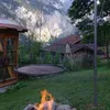 A hanging grill grate is set up in a grassy yard with a fire pit in the foreground and mountains in the background. Podgląd zdjęcia produktu