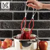 A hand holding a jar lifter, lifting a jar of jam out of a pot of boiling water. Apples are visible in the foreground. Anteprima dell’immagine prodotto