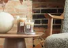Two candles are placed on a wooden table in front of a brick fireplace. Náhled obrázku produktu