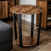A round industrial side table with a wood-look top and black metal legs is shown in a living room setting next to a dark leather sofa and a wooden cabinet. Podgląd zdjęcia produktu