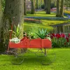 A red wooden wagon filled with plants sits on a green lawn in a garden setting with a pond and flowers in the background. Produktbild-Vorschau