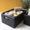 A black wooden storage box filled with spools of twine and string, placed on a white surface with a yellow background. Produktbild-Vorschau