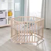 A hexagonal playpen with a mattress and a star-shaped pillow inside, set in a nursery or playroom. Produktbild-Vorschau