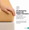 A hand is shown touching a fitted sheet on a mattress, with text overlay describing product features. Produktbild-Vorschau