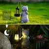 A solar-powered garden lantern shaped like a cat, shown in both daylight and nighttime settings. Produktbild-Vorschau