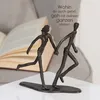 A bronze sculpture of two figures holding hands and running, with an open book in the background. Produktbild-Vorschau