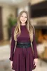 A woman is standing in a blurred indoor setting, wearing a burgundy dress and a black obi belt. Produktbild-Vorschau