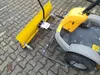 A snow plow attachment for a ride-on mower is shown on a paved surface. Produktbild-Vorschau