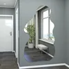 A modern hallway with a white door and a large, irregularly shaped mirror on a gray wall, reflecting a window and a plant. Produktbild-Vorschau