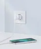 A white Anker charger plugged into a white wall socket, with a white cable connecting to a silver smartphone lying on a white surface. Anteprima dell’immagine prodotto