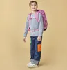 A young girl wearing a backpack and jeans stands against a plain background. Náhled obrázku produktu