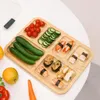 A wooden serving tray filled with various food items, including sushi, cherry tomatoes, cucumbers, and oranges, arranged on a white surface. Produktbild-Vorschau