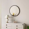 A round black framed mirror hangs on a wall above a white dresser with a lamp and two decorative cat figurines. Produktbild-Vorschau