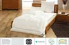 A white duvet is laid out on a wooden bed frame, with pillows behind it. A wooden dresser and nightstand are visible in the background. Produktbild-Vorschau