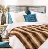 A cozy bedroom scene with a bed dressed in white linens, a plush brown and white striped throw blanket, and decorative pillows. Náhled obrázku produktu