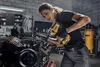 A woman is working on an engine in a workshop, using a DeWALT impact wrench. Podgląd zdjęcia produktu