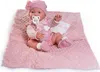 A baby doll dressed in pink, lying on a pink blanket with a bottle and pacifier. Anteprima dell’immagine prodotto