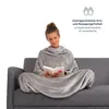 A woman is sitting on a sofa, wrapped in a gray blanket with sleeves, reading a book. Anteprima dell’immagine prodotto