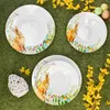 Easter-themed tableware set arranged on a grassy surface with yellow flowers. Náhled obrázku produktu