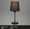 A black table lamp with a fabric shade is shown against a plain gray background. Below the lamp, there is a dark gray bar with icons and text indicating 'Switch' and 'E14 Base'. Produktbild-Vorschau
