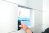 A hand is holding a laser distance measurer, measuring the depth of a cut-out in a white wall. Produktbild-Vorschau