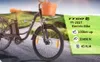 An electric bicycle with a basket in front, parked on a road with a blurred background of rolling hills. Voir les images du produit