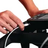 A person's hand is plugging a white USB cable into a black electronic device. Voir les images du produit