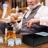 An older man in a suit is holding a glass of whiskey and a cigar, with an ice cube tray and ice cubes on a wooden table in the foreground. Náhled obrázku produktu