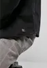 A close-up of a black shirt with a small logo tag and grey pants. Produktbild-Vorschau