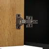 A close-up view of a cabinet hinge connecting a wooden door to a black cabinet interior. Produktbild-Vorschau