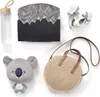 A flat lay of baby accessories including a water bottle, a stuffed koala, a round straw bag, a bib with a mountain print, and a pair of baby shoes. Náhled obrázku produktu