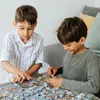 Two young boys are sitting at a table, focused on assembling a jigsaw puzzle. Produktbild-Vorschau