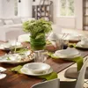A dining table set for a meal with plates, glasses, cutlery, and a floral arrangement. Náhľad obrázku produktu