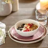 A breakfast setting with a bowl of granola and fruit on a wooden table. Produktbild-Vorschau