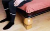 A person's legs and feet are visible, sitting on the edge of a bed. The bed is propped up by a wooden ball and a small wooden block. Podgląd zdjęcia produktu