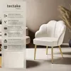 A white velvet armchair with gold legs is shown in a room with neutral-toned walls and dried grass decor. Produktbild-Vorschau