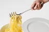 A hand is using a spaghetti server to lift pasta from a bowl onto a plate. Podgląd zdjęcia produktu