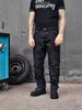 A man wearing work pants and a t-shirt stands in front of a garage door with a tire and a tool cart. Produktbild-Vorschau