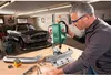 A man is working on a car part with a drill press in a garage. Podgląd zdjęcia produktu