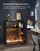 A dark, modern interior with a cabinet filled with bottles and jars, illuminated by soft lighting. A table and chair are visible in the background. Produktbild-Vorschau