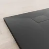 A close-up view of a black shower tray with a textured surface, resting on a light-colored wooden floor. Produktbild-Vorschau