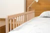 A close-up view of a wooden bed rail on a bed with white bedding. Voir les images du produit
