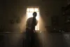 A person stands in a dimly lit kitchen, illuminated by a bright light streaming through a window. Náhľad obrázku produktu