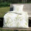 A bedding set with a botanical print is displayed on a wooden bench outdoors, with grass and foliage in the background. Produktbild-Vorschau