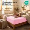 A woman sleeping on a bed with a pink fitted sheet. Produktbild-Vorschau