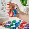 A hand holding a set of resin letter molds and keychains, with more molds laid out on a tray. Produktbild-Vorschau