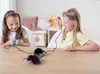 Two young girls playing with toy spiders on a wooden table. Produktbild-Vorschau